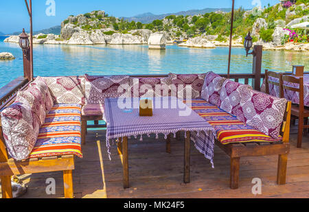 The coastal patio of the restaurant with nice view on ancient Lycian tomb, standing in shallow waters of Kekova Bay, Kalekoy, Turkey. Stock Photo