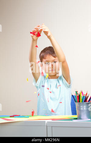 Child throwing small piece of colored paper as confetti after he created greeting card Stock Photo