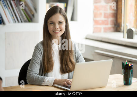 Smiling female worker posing while working at laptop Stock Photo