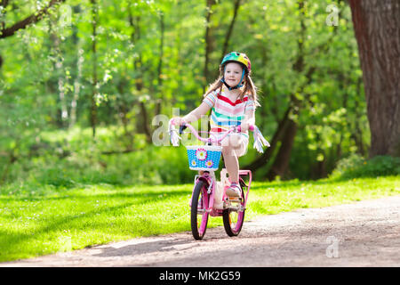 Child riding a bike in summer park. Little girl learning to ride a bicycle without training wheels. Kindergarten kid on two wheeler bike. Active outdo Stock Photo