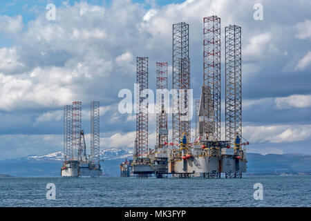 CROMARTY FIRTH SCOTLAND GROUP OF TALL STRUCTURED OIL RIGS UNDERGOING REPAIR LYING OFF CROMARTY VILLAGE WITH SNOW COVERED HILLS
