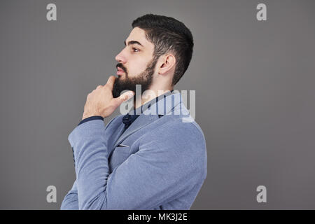 Portrait of freelancer man with beard in jacket standing against gray backdrop Stock Photo