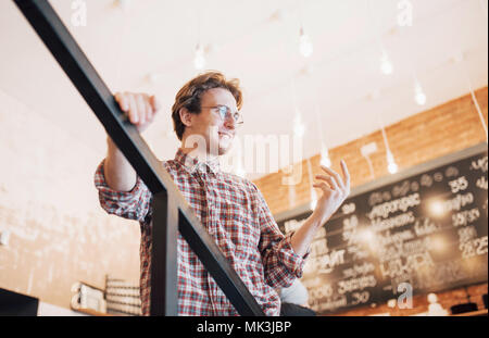 Thoughtful young man is sitting in confectionery shop. She is drinking coffee while waiting for someone Stock Photo