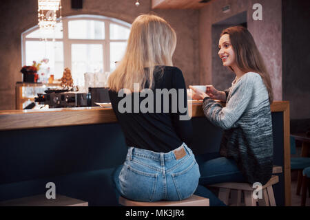 communication and friendship concept - smiling young women with coffee cups at cafe Stock Photo