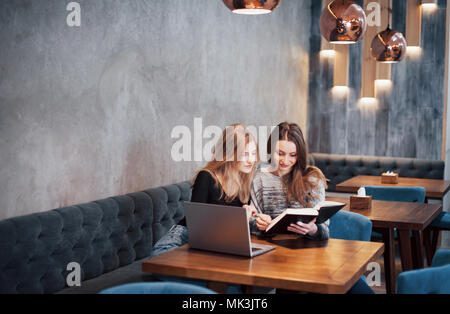 One-on-one meeting.Two young business women sitting at table in cafe.Girl shows colleague information on laptop screen.Meeting friends, dinner together.Teamwork, business meeting. Freelancers working Stock Photo