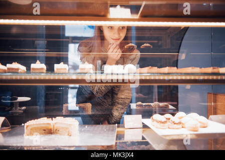 Smiling woman at camera through the showcase with sweet and cakes in modern cafe interior Stock Photo