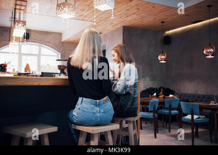 Two smiling friends reading funny online chat on modern telephone sitting with tasty coffee in restaurant.Hipster girls enjoying recreation time in cafe with hot beverages and messaging on cellular Stock Photo