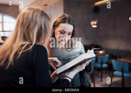 Two young women sitting in the cafe drinking coffee and enjoying in good books. Students on coffee break. Education, lifestyle concept Stock Photo