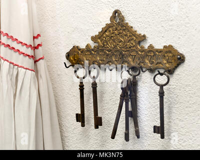 A vintage set of ornate brass keys hanging from an intricately designed key holder on a textured wall, Stock Photo