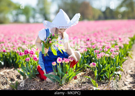 Child in tulip flower field with windmill in Holland. Little Dutch girl in traditional national costume, wooden clogs, dress and hat, with flower bask Stock Photo