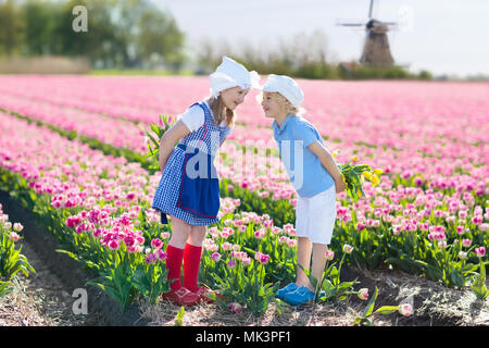 Children in tulip flower field with windmill in Holland. Little Dutch girl and boy in traditional national costume, wooden clogs and hat, with flower  Stock Photo