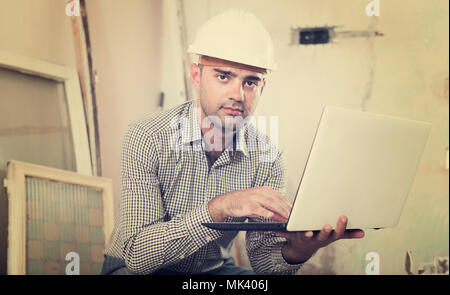 Portrait of master working at the notebook in shirt and helmet Stock Photo