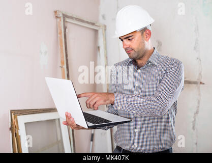 Adult man engineer managing process with laptop in helmet indoors Stock Photo