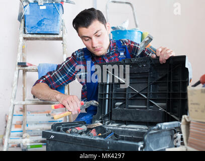 Young builder handyman choosing necessary tool in toolbox Stock Photo