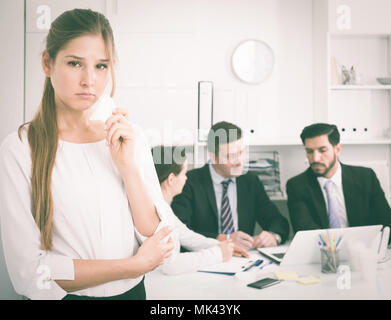 Unhappy and crying woman standing at office on background with coworkers Stock Photo