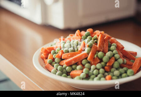 frozen vegetables on plat near mocrowave, kitchen indoor. Vegan food Stock Photo