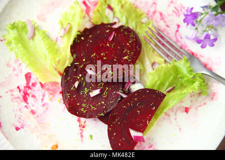 Beet slices with red onion bits, lettuce and grated lime zest on a beet juice-stained plate Stock Photo