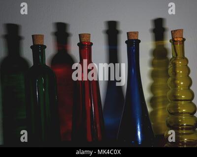Illuminated coloured bottles casting shadows on wall. Stock Photo