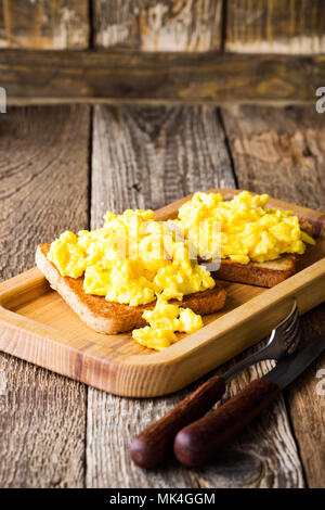 Scrambled eggs on two pieces of toast on wooden table, healthy and delicious breakfast Stock Photo