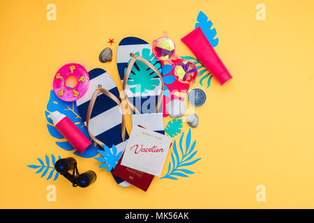 Summer vacation accessories, sunglasses, flip-flops, sunscreen, tiny swim ring, shells on a vibrant yellow background. Traveling essentials flat lay with copy space. Feminine blue and pink palette. Stock Photo