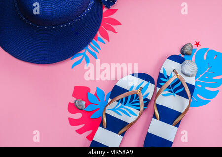 Beach accessories, flip flops, tropical leaves, broad-brim, seashells flat lay. Colorful travel and vacation concept on a feminine pink background with copy space. Stock Photo