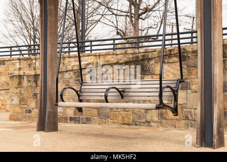 bench pergola in park alongside stone brick wall on gravel walkway Stock Photo