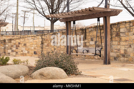 bench pergola in park alongside stone brick wall on gravel walkway Stock Photo