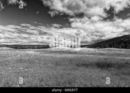 Empty grass field with hills to one side under a cloudy sky, black and white. Stock Photo