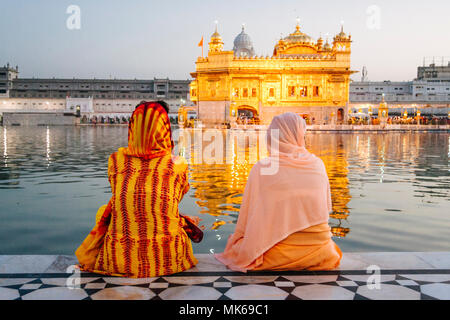 Amritsar, Punjab, India : Two Sikh pilgrim women sit looking at the Golden Temple illuminated at dusk. Stock Photo