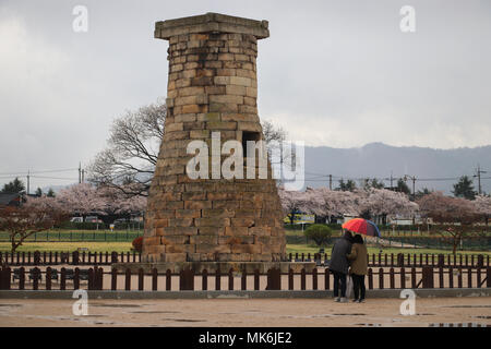 Two people with a red umbrella view the 1350 year old Cheomseongdae Observatory, oldest surviving in Asia, on a rainy day in Gyeongju, South Korea. Stock Photo