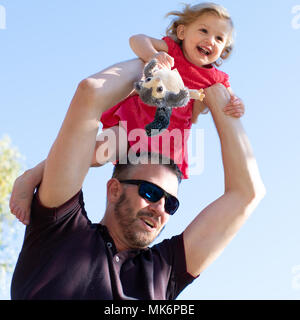 A father lifts his daughter above his head during a family photoshoot in a park Stock Photo