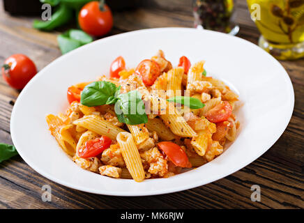 Penne pasta in tomato sauce with chicken, tomatoes, decorated with basil on a wooden table. Italian food. Pasta Bolognese. Stock Photo