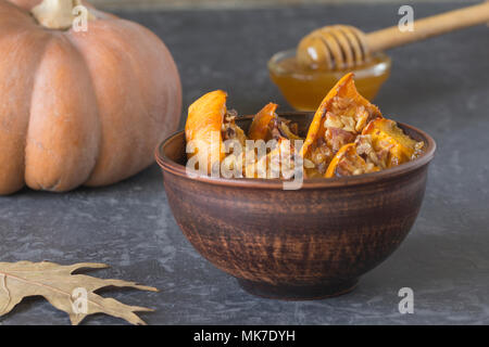 Authentic view of the baked sliced pumpkin with honey and walnuts in a ceramic bowl (pial) on a dark gray background. Close-up. Stock Photo
