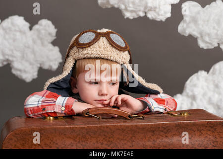 boy dressed as an airplane pilot sit between the clouds with old suitcase and dreams Stock Photo