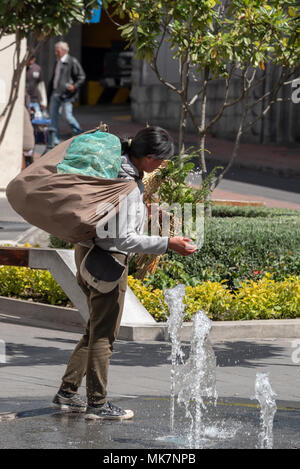 Street vendor splashing water from a fountain onto plants she's selling in the historic old city of Quito, Ecuador. Stock Photo