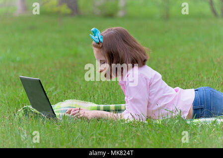 girl child with laptop outdoors resting on green grass Stock Photo