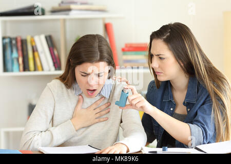 Student helping to her asmathic friend giving the inhaler during an asthma attack Stock Photo