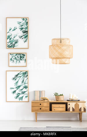 Rattan lamp above wooden cupboard against white wall with posters in simple living room interior Stock Photo
