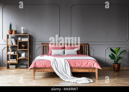 Bright blanket on pink bedding of wooden bed in grey bedroom interior with plant Stock Photo