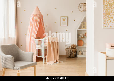 Wooden crib with dirty pink canopy standing in bright nursery room interior with grey chair and windows Stock Photo Alamy