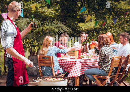 Happy cook drinking beer and grilling food during meeting with friends at barbeque party Stock Photo