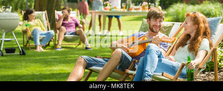 Young man playing guitar music for a girl during barbecue party Stock Photo