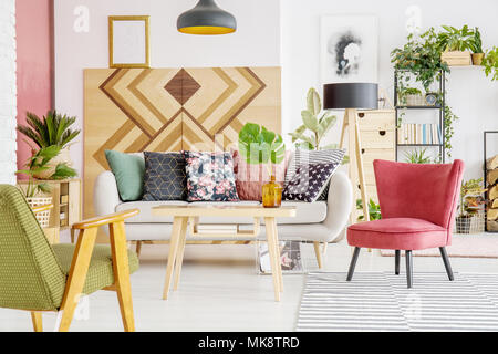 Armchairs, sofa with patterned cushions and wooden wall in a living room interior Stock Photo