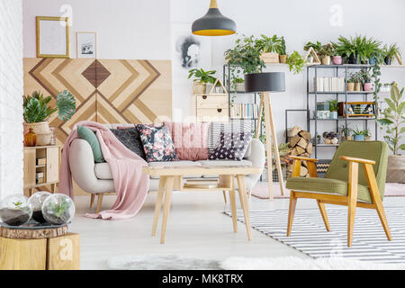 Botanical living room interior with comfy couch and pillows, armchair, wooden coffee table and wall Stock Photo