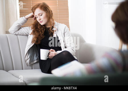 Depressed woman drinking coffee during psychotherapy in the office Stock Photo