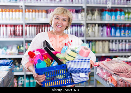 Mature housewife holding basket with chemical products for cleaning home in store Stock Photo