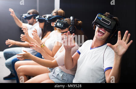 Happy young guy with friends wearing VR headset, interactive touching over air Stock Photo