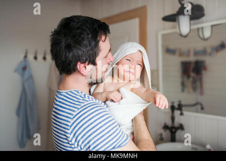 Father with a toddler child wrapped in towel in a bathroom at home. Stock Photo