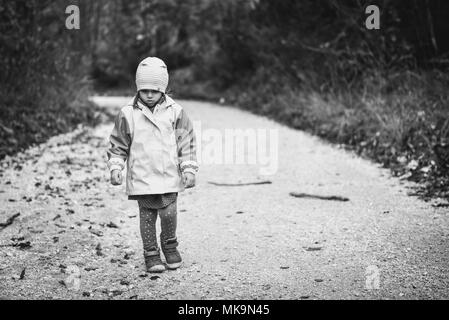 Young sad girl child is walking alone on country road. Abandoned sad little girl is walking in nature and looking down. Concept of loneliness, abandon