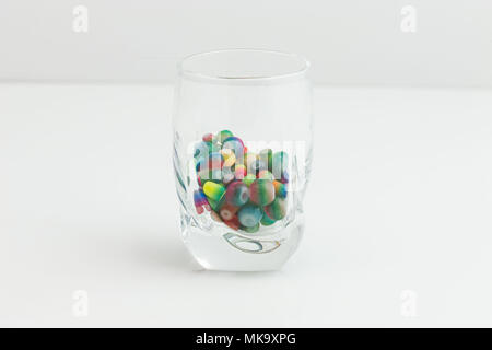 multi colored and shaped jewelry beads in a small clear glass on white Stock Photo